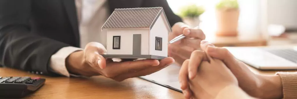 corretor de imóveis apontando miniatura de casa para mulher