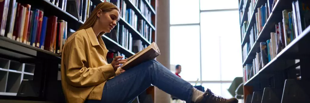 menina sentada no chão lendo em biblioteca